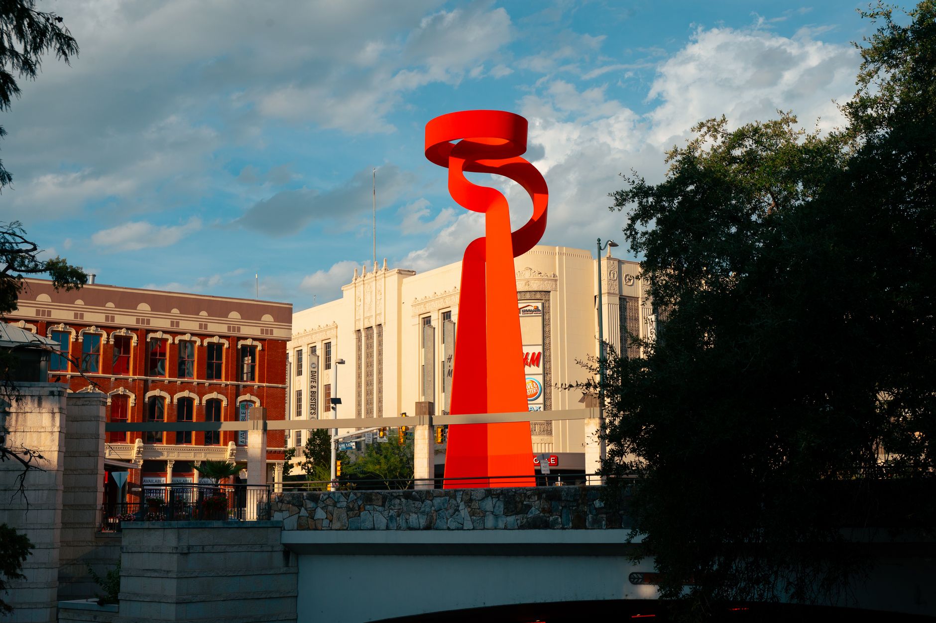 Striking red modern sculpture in a cityscape with historic buildings under a blue sky.