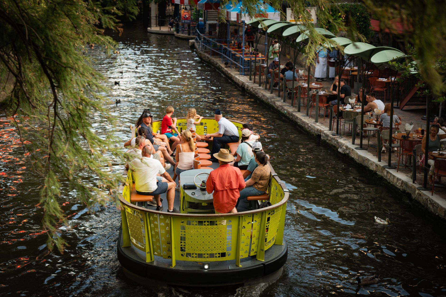 Tourists enjoy a scenic boat tour on a vibrant riverwalk lined with cafes.